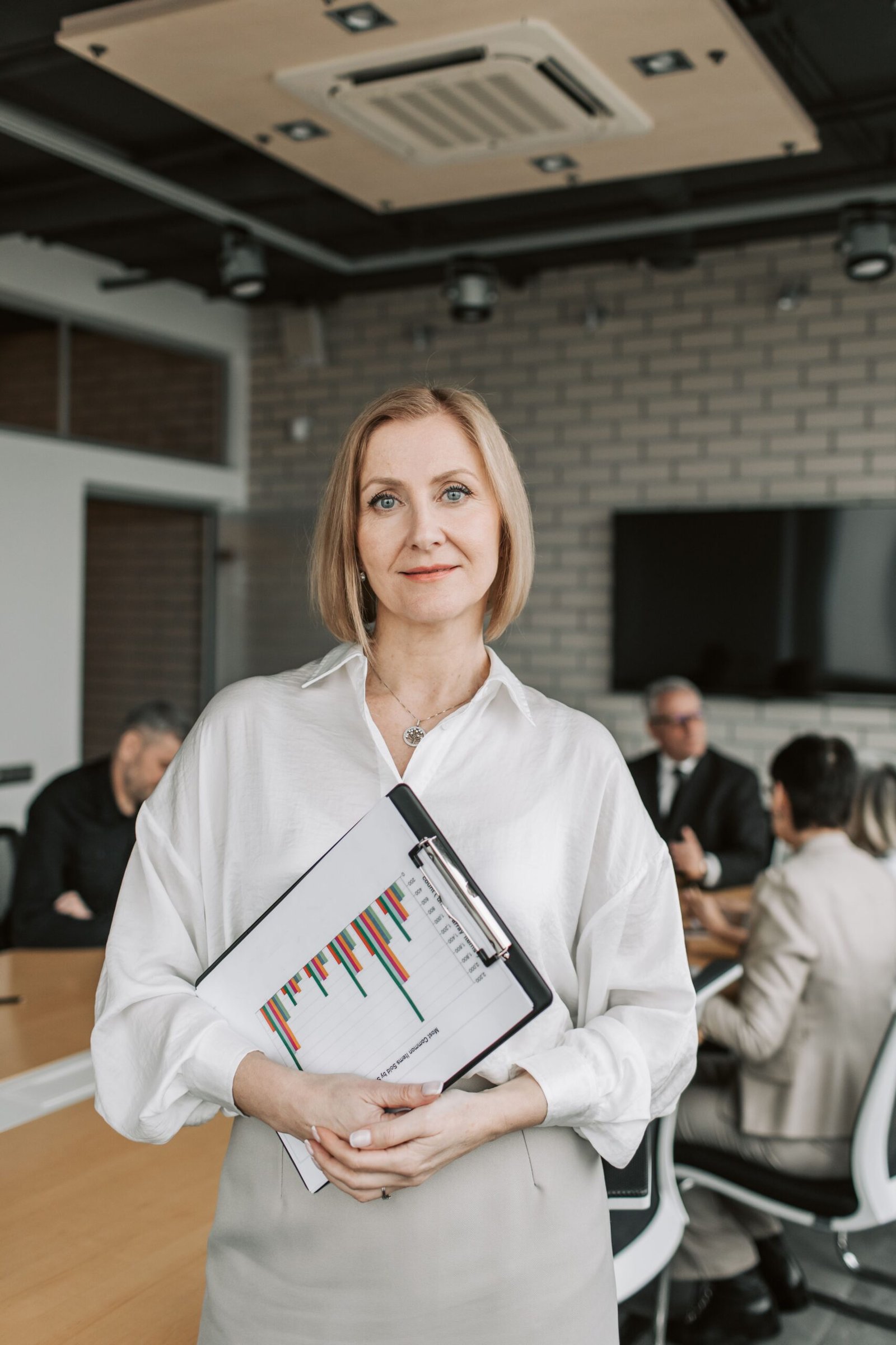Professional woman holding clipboard in corporate office setting during a business meeting.